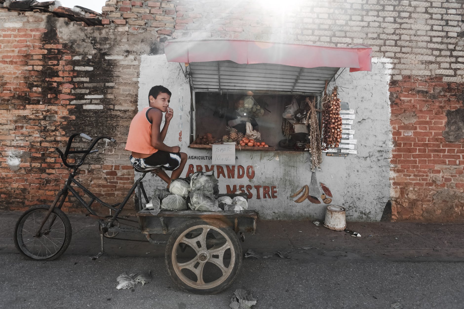 ethnic boy sitting on aged tricycle near poor street stall
